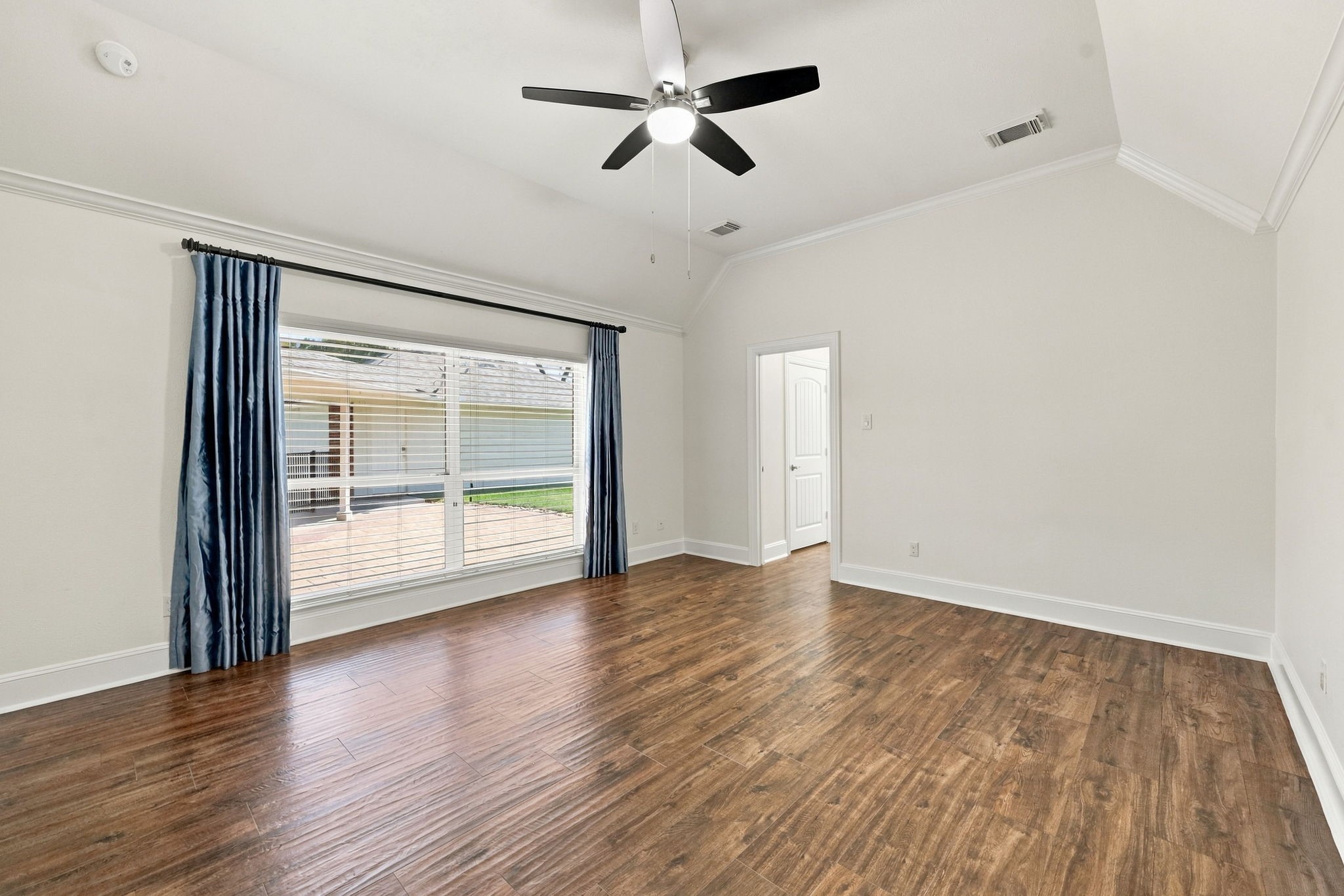 The spacious Primary Suite easily accommodates a king-size bed with two side tables, along with a comfortable seating area. The room features beautiful wood-look tile flooring, elegant crown molding, 5-inch baseboards, two large windows dressed with designer drapes and 2-inch blinds, a 5-blade ceiling fan, and beautiful views overlooking the back patio.