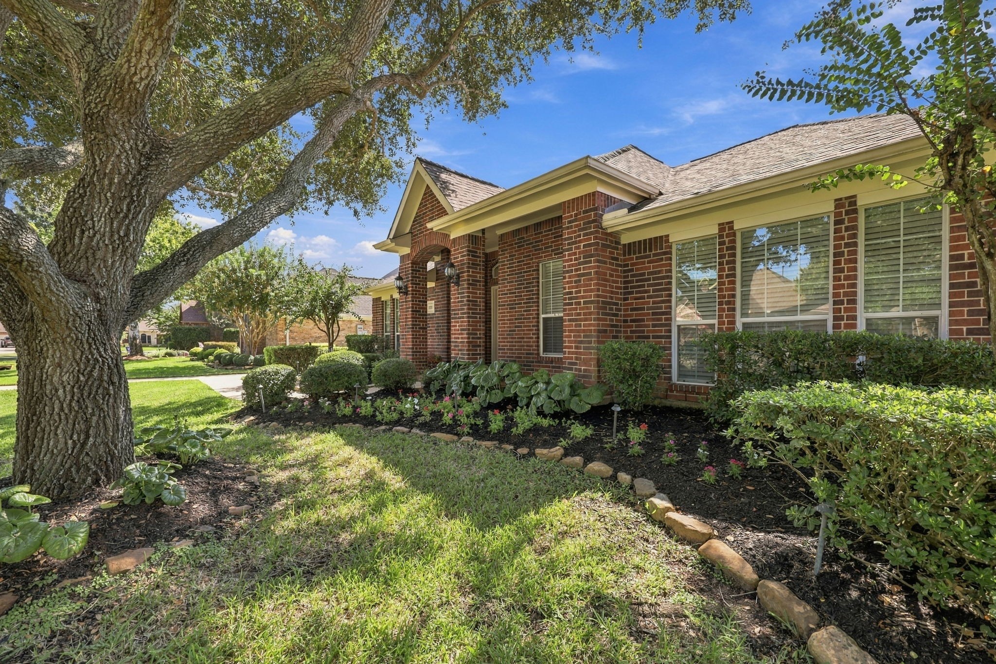 The mature landscaping is beautifully bordered with natural stone and features a variety of lush shrubs and greenery, creating a warm, inviting, and well-manicured setting that enhances the homes exceptional curb appeal.