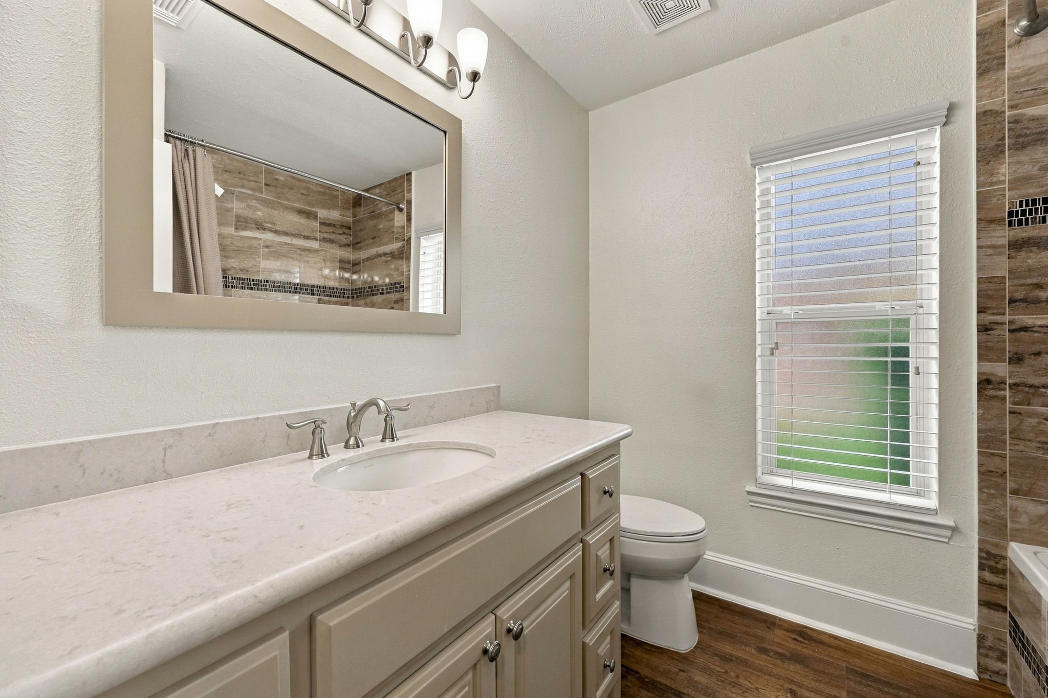 This Full Bath serves the two Secondary Bedrooms featured in the previous photos and is beautifully appointed with Quartz countertops, an undermount sink, a framed mirror, widespread brushed nickel faucet, and coordinating light fixture and hardware. Elegant finishes create a stylish and cohesive space.