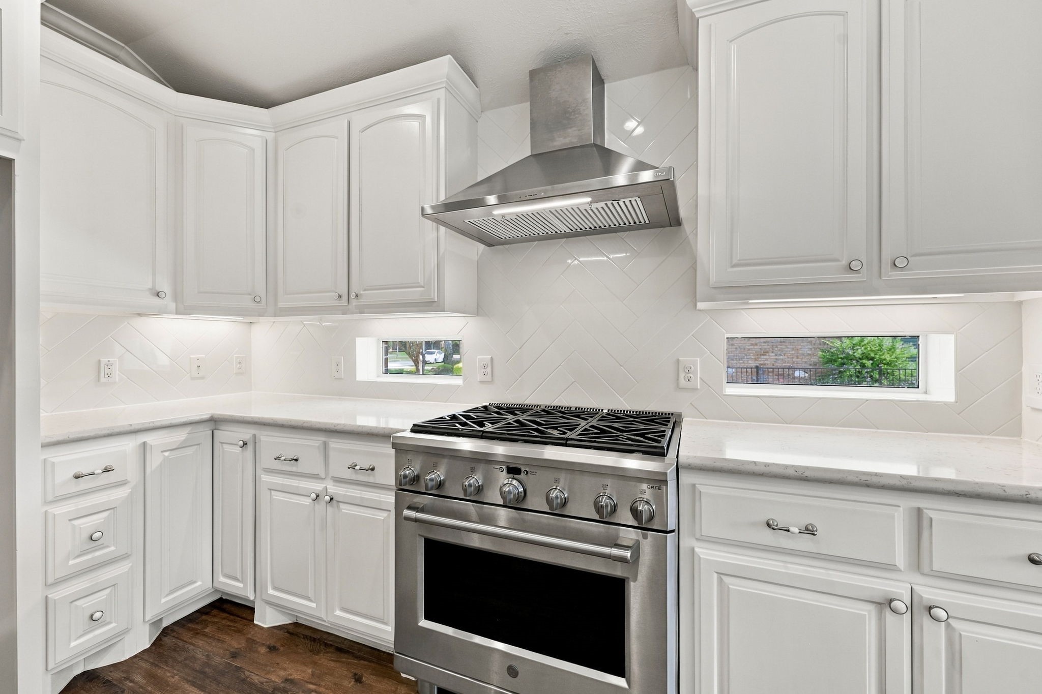 The commercial-grade GE Caf 6-burner gas range with electric oven is a chefs dream, complemented by a sleek stainless steel vent hood above. Two elegant windows on either side fill the space with natural light, while the gorgeous subway tile backsplash, beautifully set in a herringbone pattern, adds a stylish finishing touch.