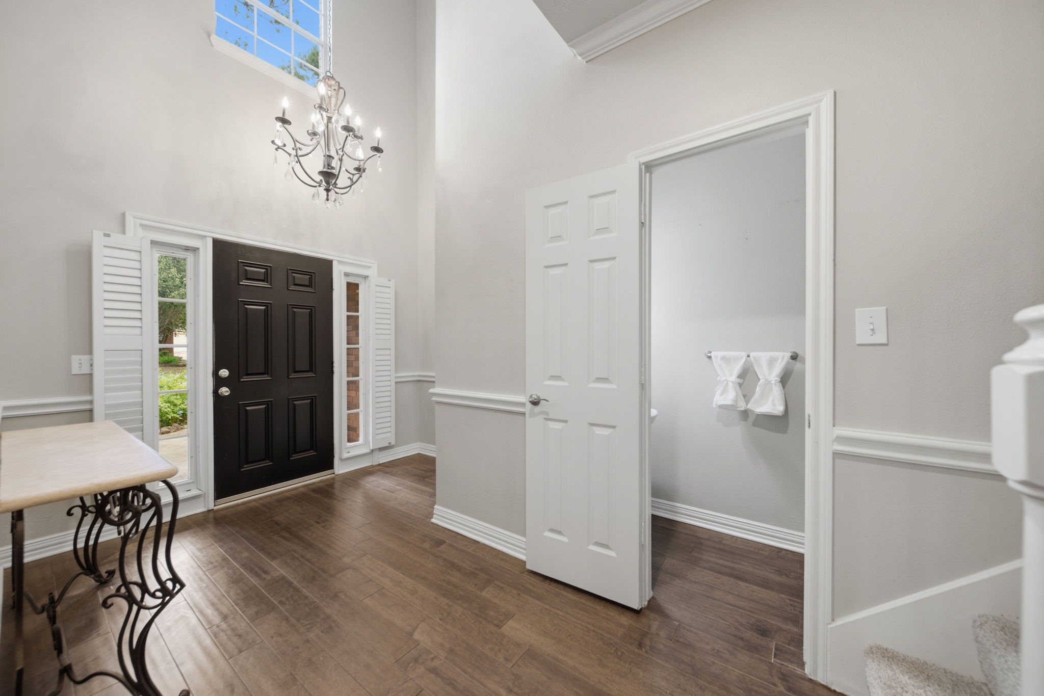 Elegant entryway featuring a grand chandelier, high ceilings, and rich wood flooring, with convenient access to the powder room.