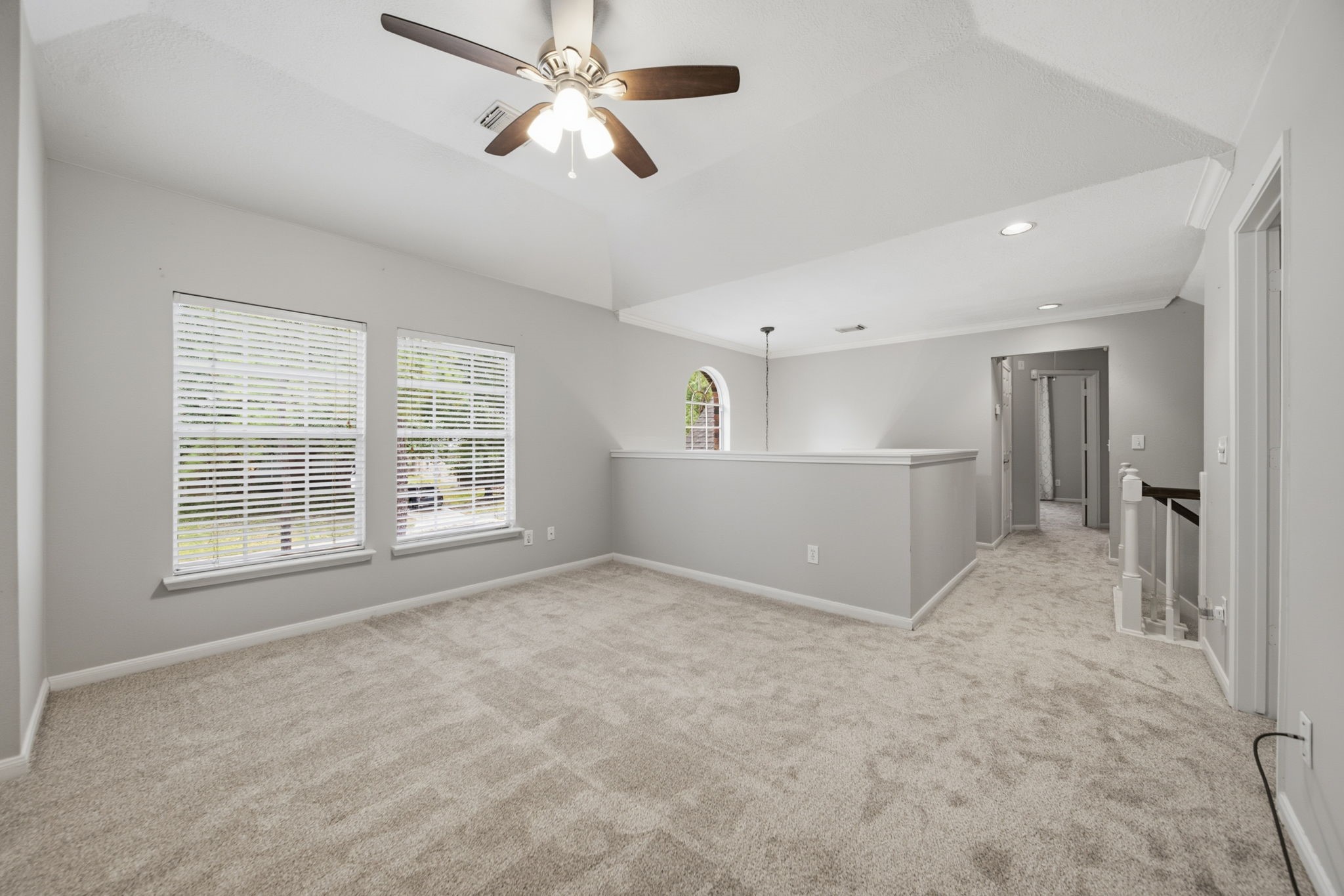 The upstairs game room offers a versatile space for games, movie nights, toys, or a second living area. High ceiling, neutral decor, and two large windows create a bright, open feel, while a ceiling fan adds comfort to this inviting gathering space.