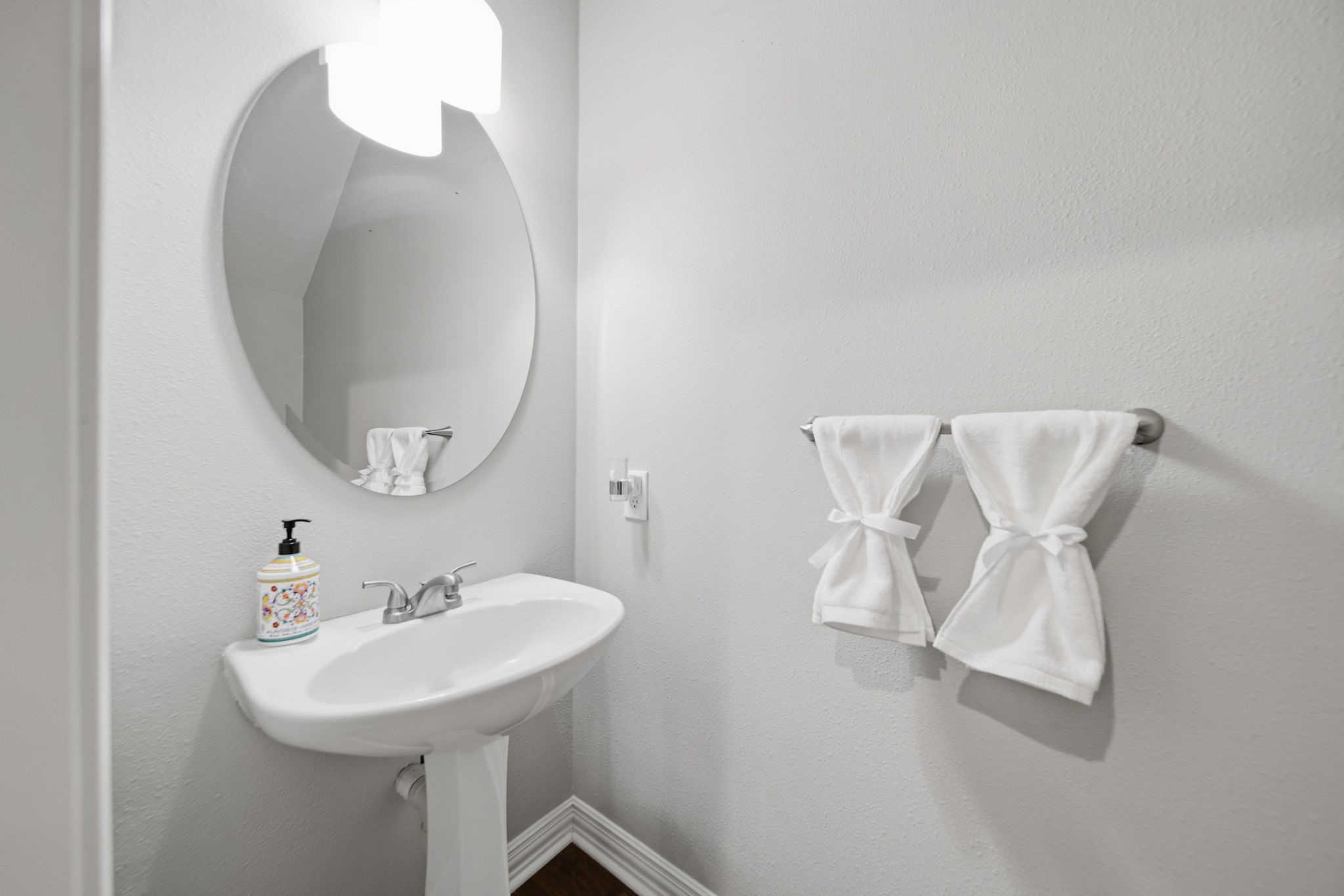 Charming powder room with a sleek pedestal sink, elegant oval mirror, and modern lighting.