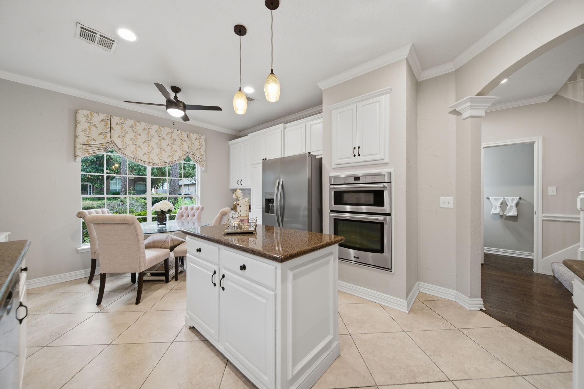White cabinetry, stainless steel microwave and oven, and pendant lighting complement this inviting kitchen. The center island provides addional prep and storage space. The adjoining breakfast area offers natural light and views of the greenery outside. Custom window treatments nicely frame the large window.