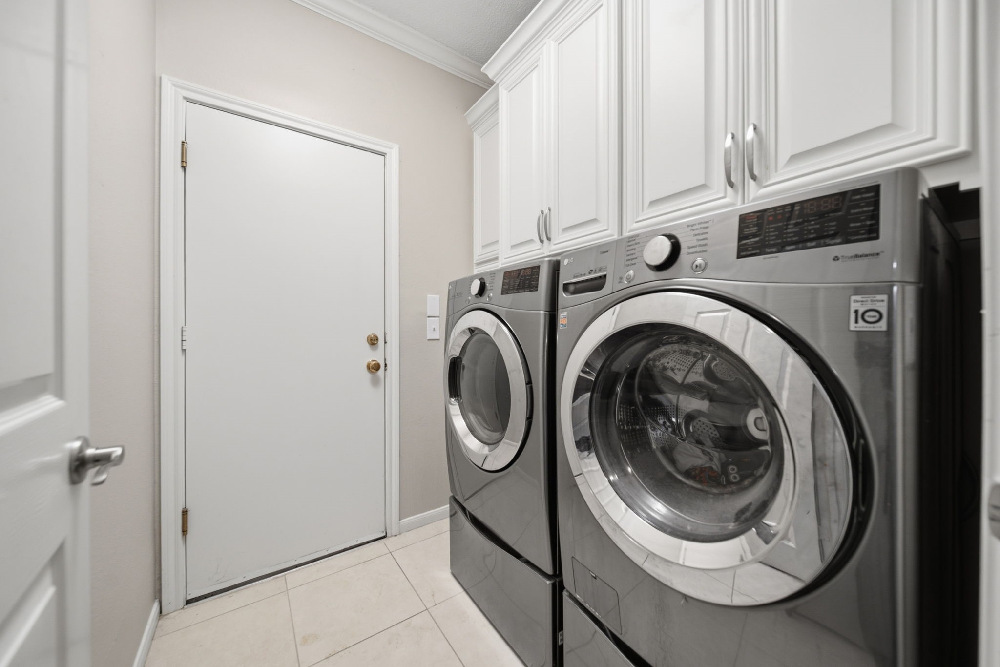 Added cabinetry surrounds the included washer & dryer, providing generous storage and a custom finished look in this well-organized laundry room. An additional storage closet is tucked behind the door in the foreground, offering convenient space for household essentials.