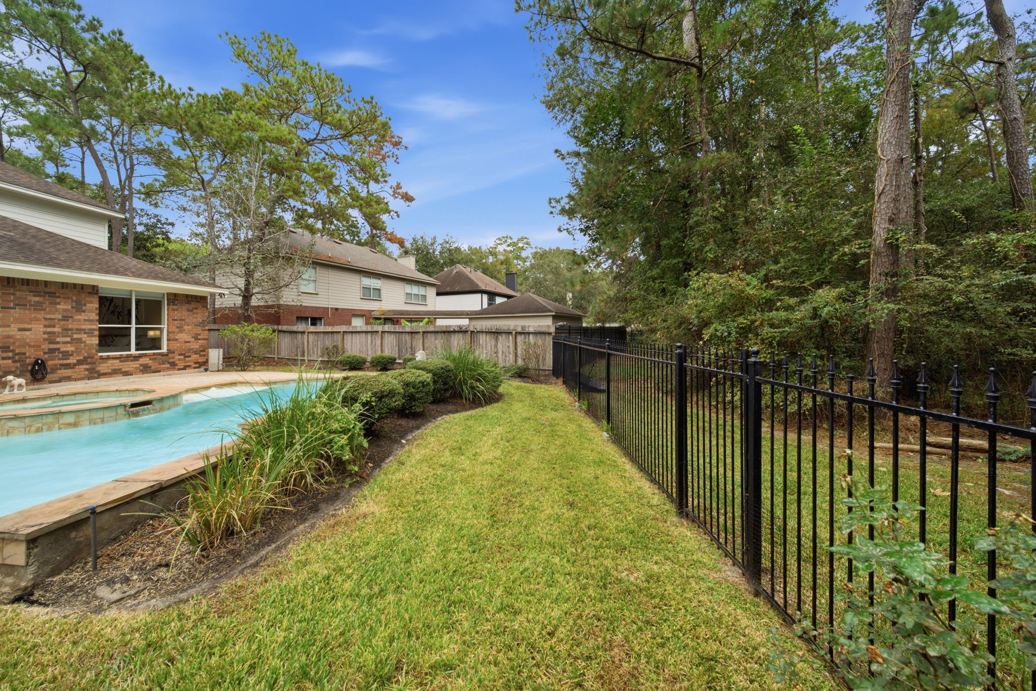 Enjoy peaceful wooded views through the wrought iron fence in this inviting back yard. The sparkling pool, landscaped beds, and grassy areas create a beautiful setting for outdoor relaxation and watching nature.