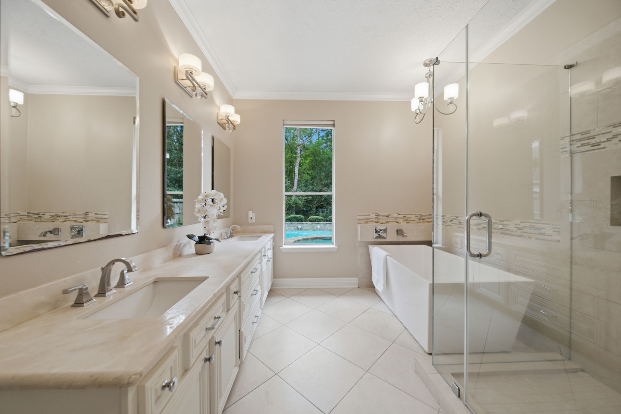 This beautifully updated master bath features a freestanding soaking tub, separate frameless glass shower, and an expansive double-sink vanity with white cabinetry and generous storage. The updated lighting, soft neutral finishes, and natural light create an inviting retreat for you after a long day.
