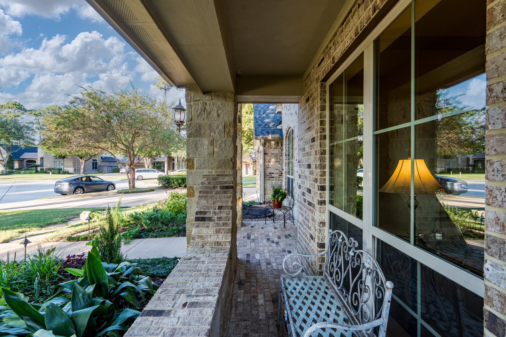 A CHARMING PLACE TO PAUSE AND ENJOY THE BEAUTY OF HOME! This inviting covered front porch features beautiful brick detailing, stately stone columns, and an elegant wrought-iron bench overlooking lush landscaping and the picturesque neighborhood. A peaceful spot to enjoy your morning coffee, welcome guests, or simply savor the timeless charm of this exceptional home!