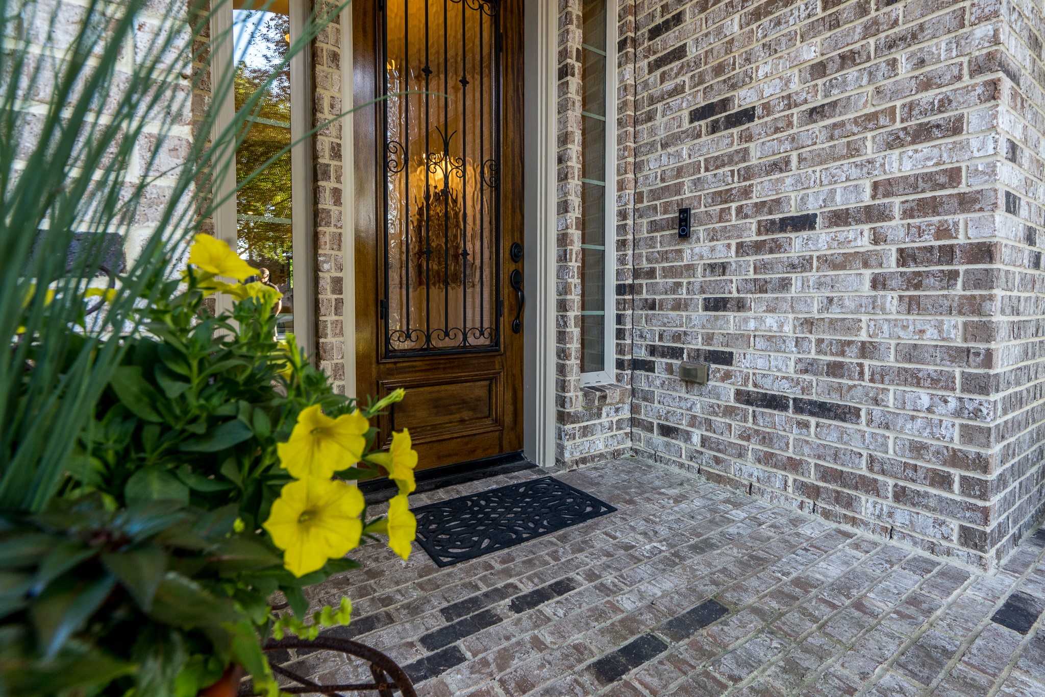 WHERE ELEGANCE BEGINS AT THE FRONT DOOR! A beautifully crafted wood entry door with exquisite wrought-iron detailing welcomes you home, framed by timeless brickwork and charming sidelights. Vibrant seasonal blooms add a delightful touch of color, offering a glimpse of the warmth, sophistication, and attention to detail awaiting inside this exceptional J. Patrick semi-custom home!