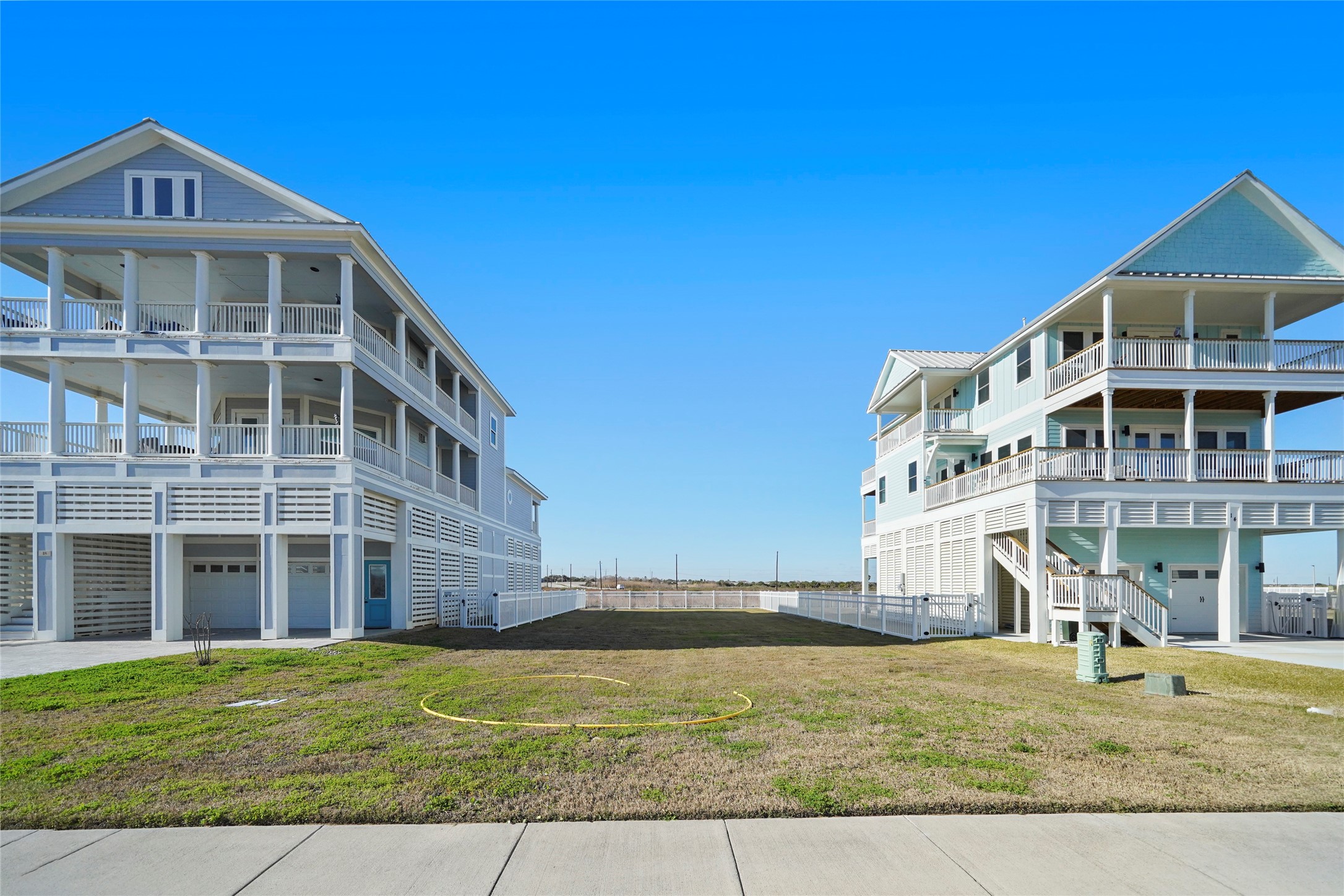 Street-level view from the homesite toward the Gulf demonstrates the property's close relationship to the water and the scale of the neighboring coastal residences. The cleared 50' 120' lot is positioned between two existing homes, providing a valuable real-world reference for the size and potential massing of a future residence. Street-level view from the homesite toward the Gulf demonstrates the property's close relationship to the water and the scale of the neighboring coastal residences. The cleared 50' 120' lot is positioned between two existing homes, providing a valuable real-world reference for the size and potential massing of a future residence.