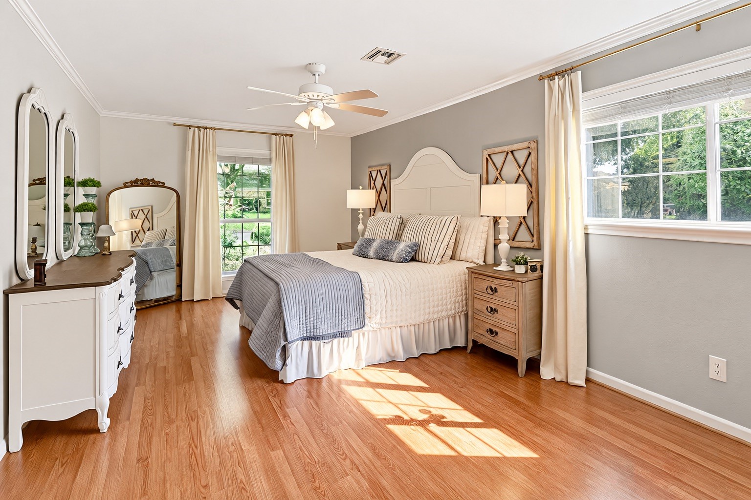 Inviting first-floor primary suite featuring beautiful flooring, abundant natural light, a ceiling fan, and generous space for comfortable furnishings.
