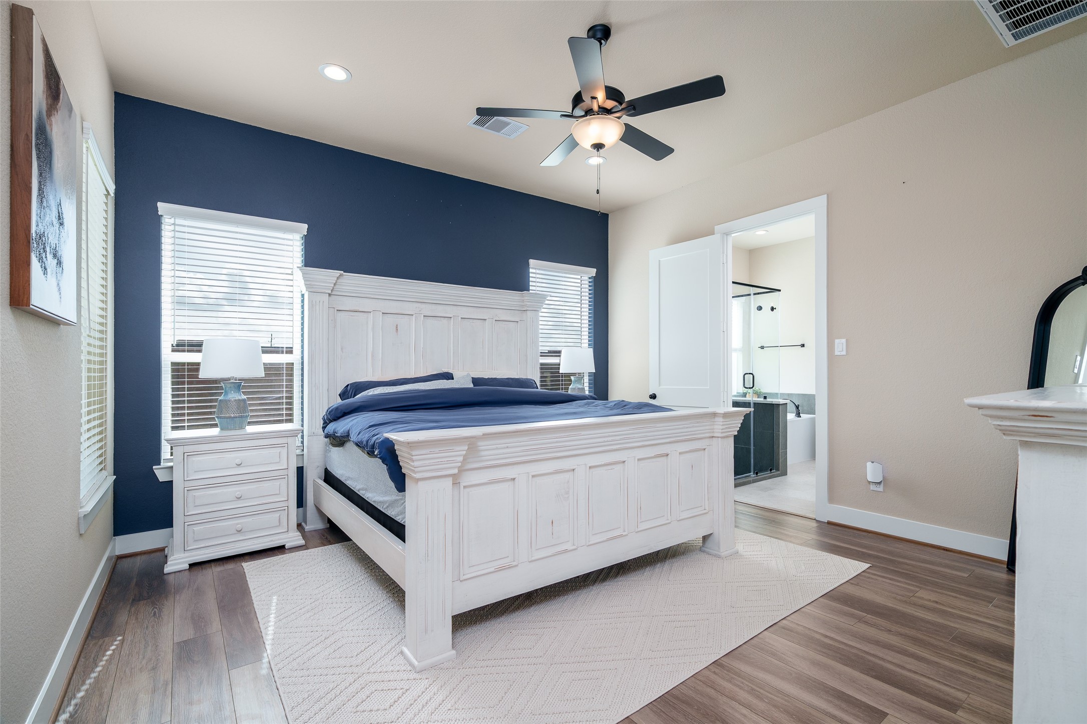 Retreat to the serene primary bedroom, featuring windows with privacy blinds, elegant vinyl plank flooring, custom accent wall, and a stylish ceiling fan for ultimate comfort and relaxation!