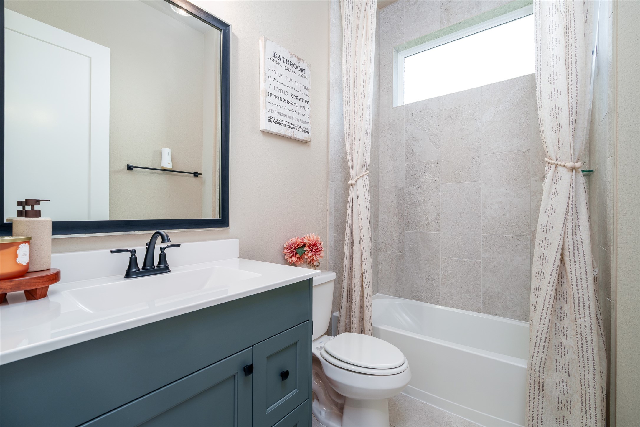 This well-appointed bathroom features a convenient shower/tub combo, a sleek custom painted vanity with a framed mirror, and a modern toilet, providing both style and functionality.