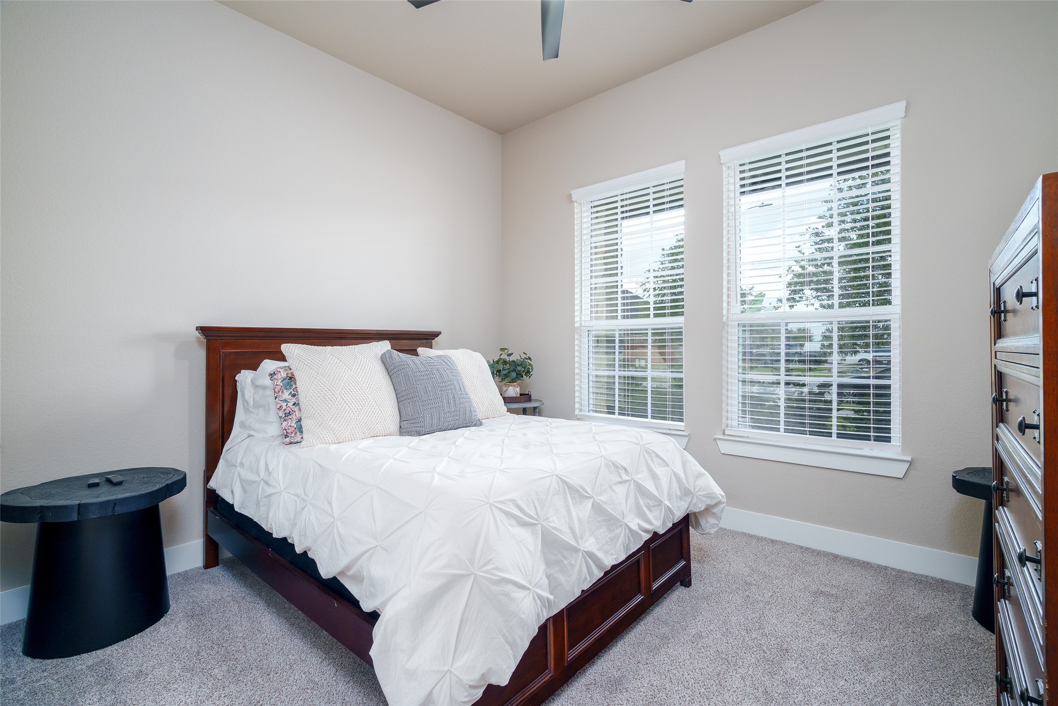 This charming bedroom features soft carpet flooring, a ceiling fan for added comfort, and a window with privacy blinds to let in natural light while maintaining your personal space.