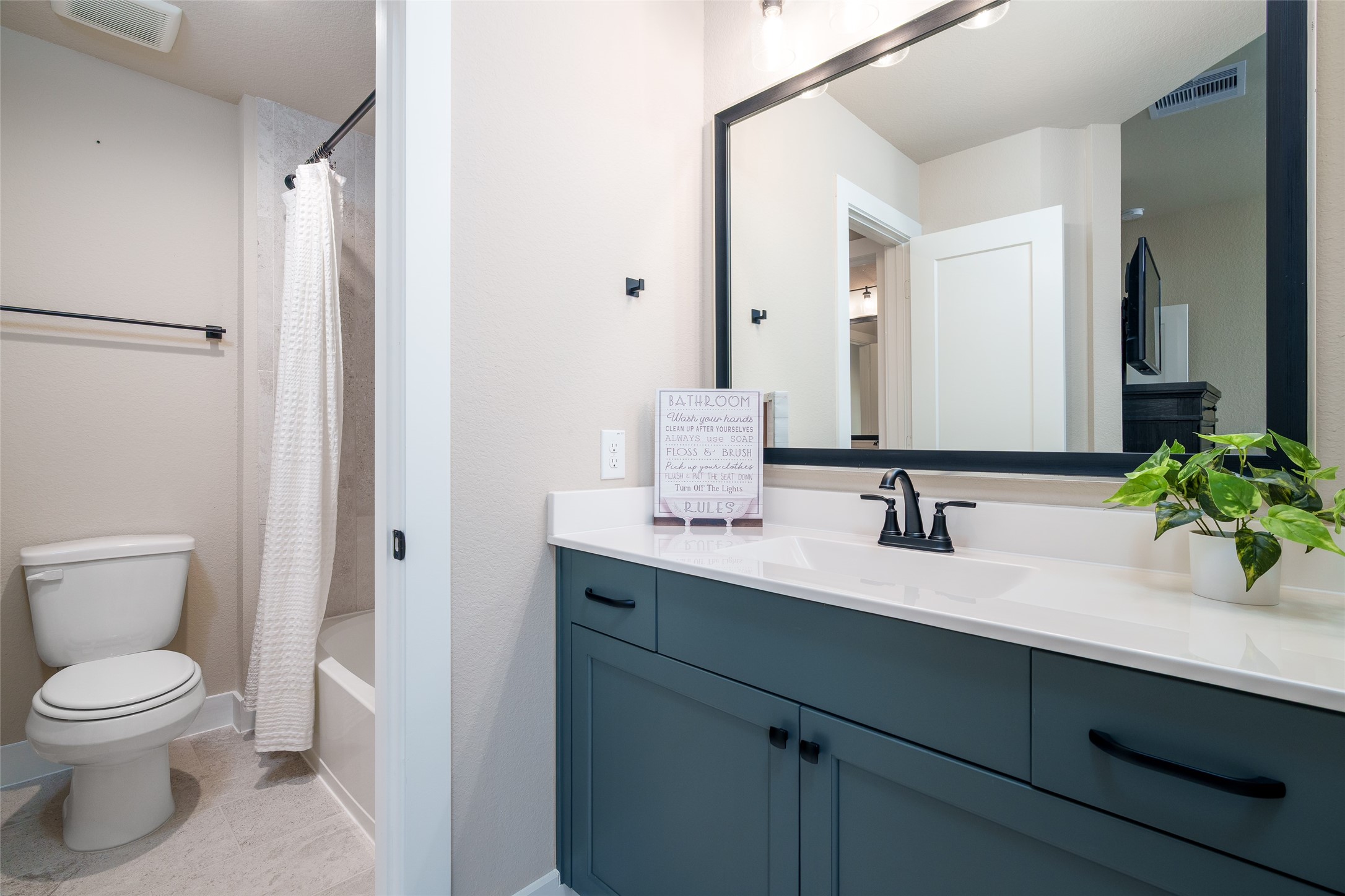 This bedrooms private sink area showcases a custom-painted vanity with a framed mirror, that conveniently connects to a shared bathroom featuring a shower/tub combo and toilet, providing comfort and ease for daily living.