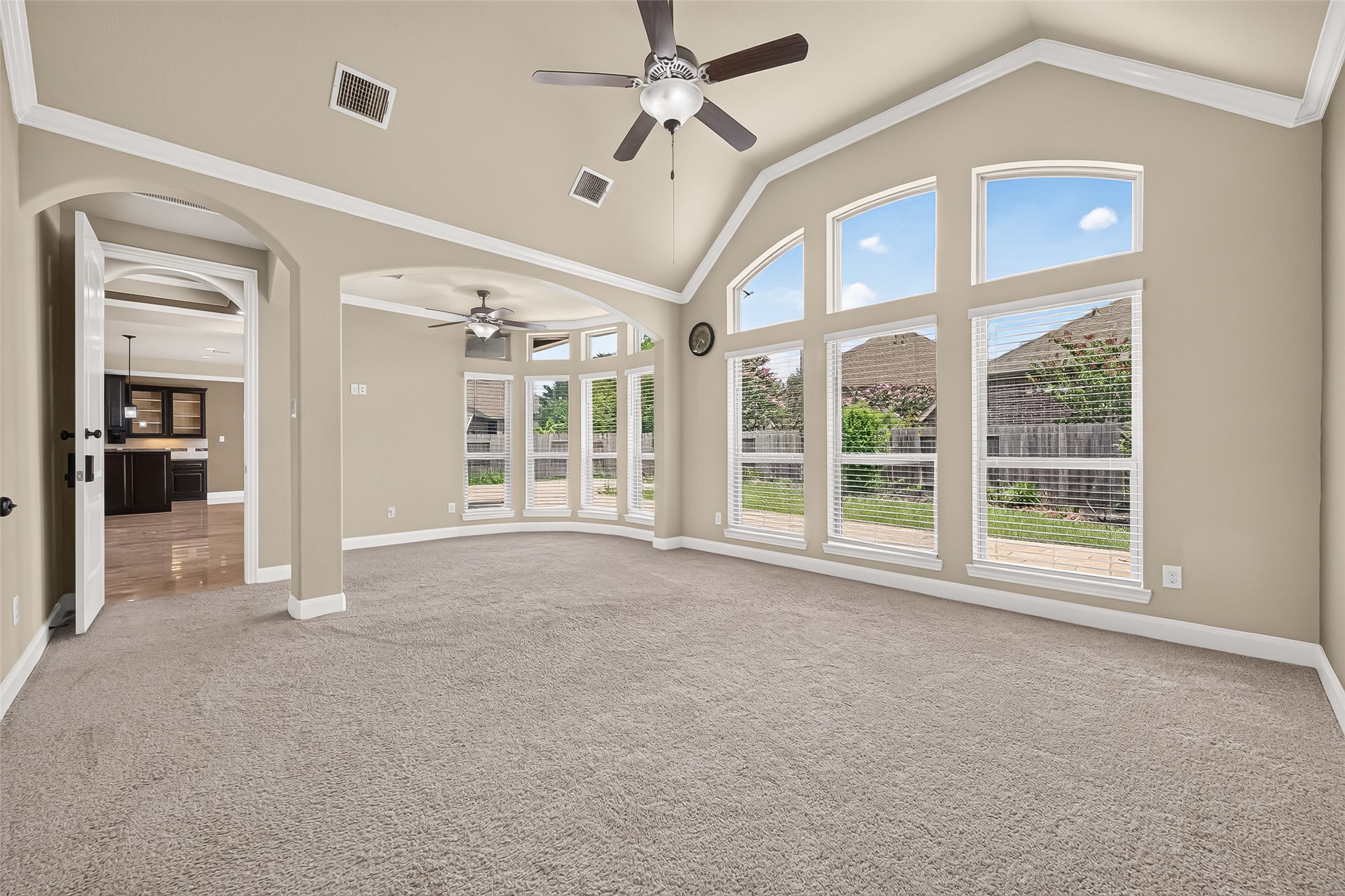 Primary Bedroom: Privately situated at the rear of the home, the luxurious primary suite offers high ceilings, plush carpet, a cozy sitting area, arched walkways, and a wall of windows that brings in abundant natural light.