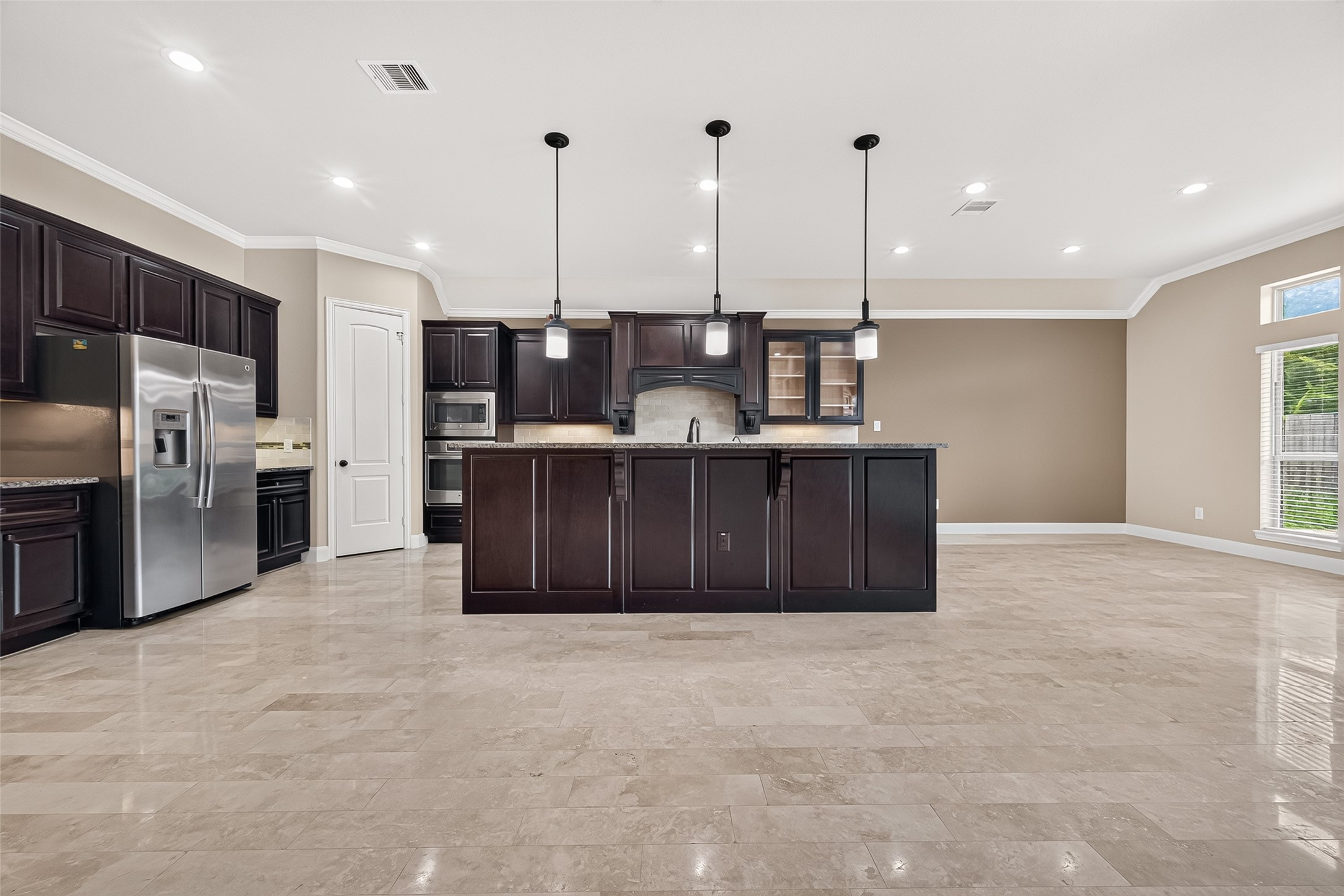 Kitchen: The open-concept island kitchen is designed for both everyday living and entertaining, featuring granite countertops, pendant lighting, rich dark wood cabinetry with upgraded display cabinets, extensive countertop space, built-in stainless steel appliances, a gas cooktop, and a beautiful tile backsplash with decorative accent tiles.
