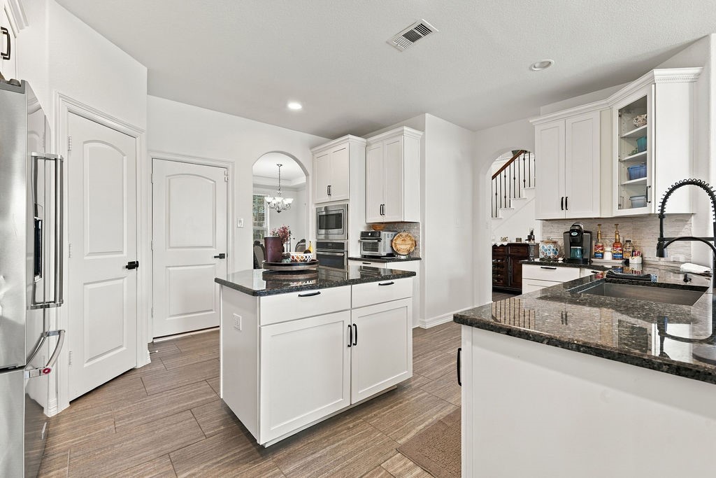 Modern kitchen with sleek white cabinetry, granite countertops, and a central island. Stainless steel appliances and an open layout enhance functionality and style.