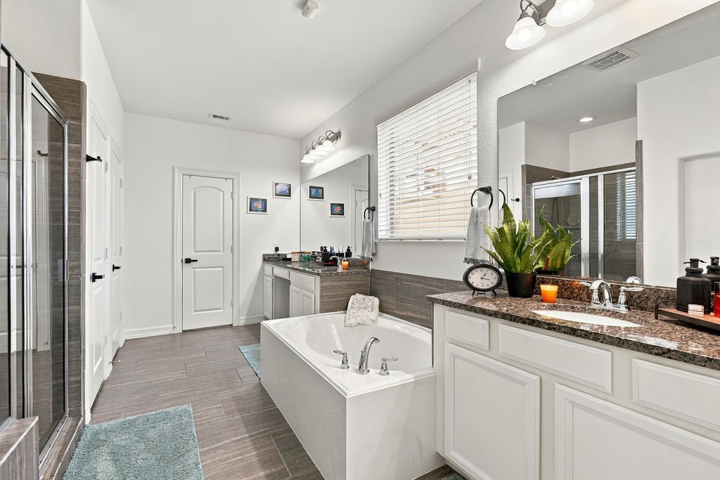 Elegant bathroom featuring a spacious soaking tub, dual sinks with granite countertops, and a walk-in shower, all accented by modern fixtures and abundant natural light.