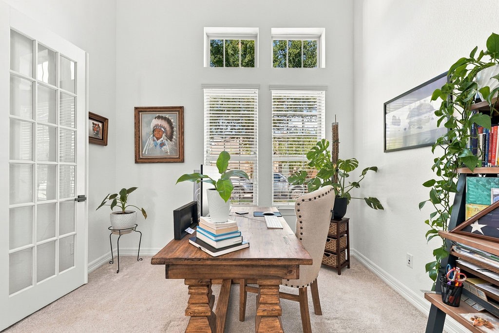 Bright and inviting home office with high ceilings, large windows, and French doors, featuring stylish decor and abundant natural light.