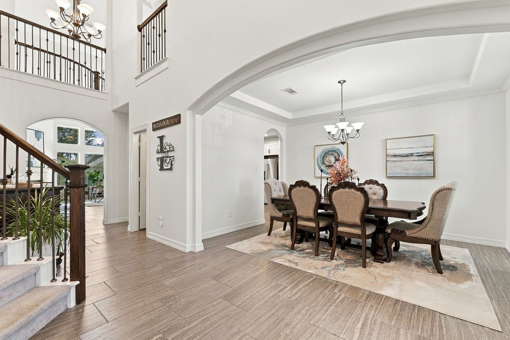 Elegant dining area with a sophisticated chandelier, beautifully set beneath a coffered ceiling, adjacent to a grand staircase with wrought iron railings.
