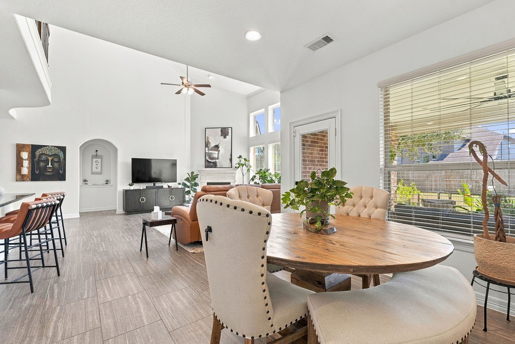 Spacious and bright open-concept living area with high ceilings, featuring a cozy seating arrangement, elegant breakfast space, and modern kitchen bar, all beautifully lit by large windows.