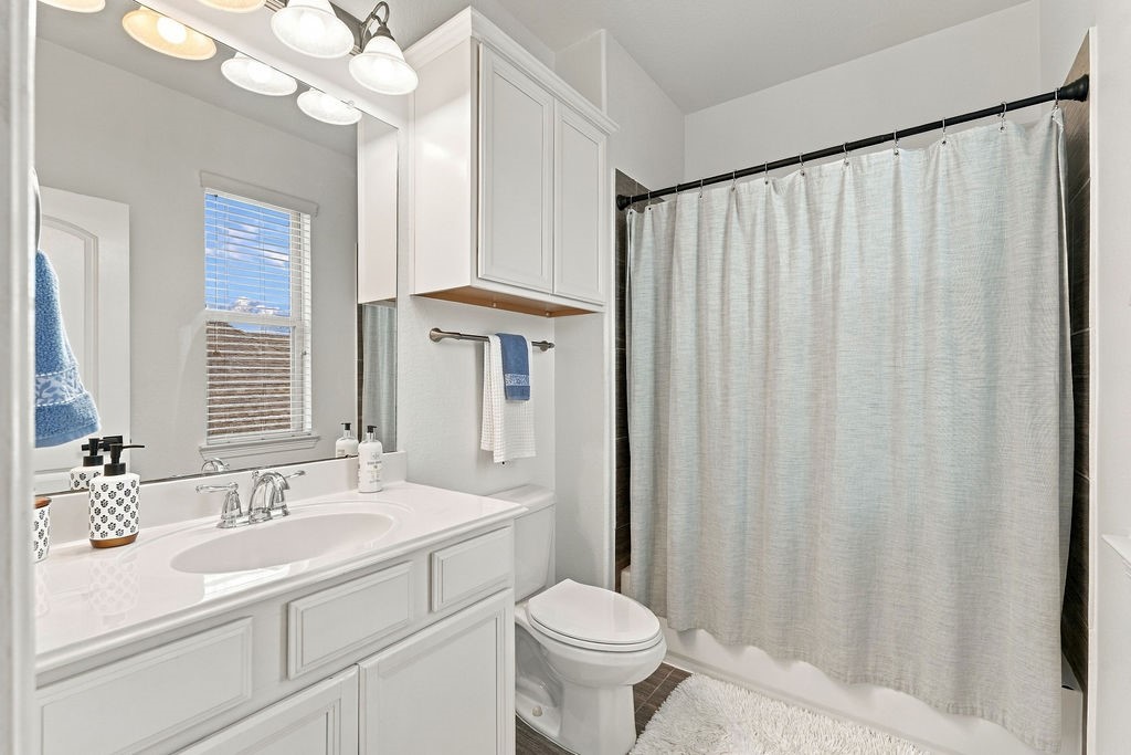 Bright and inviting bathroom featuring sleek white cabinetry, a modern vanity with ample counter space, and a full shower-tub combo with a stylish curtain.