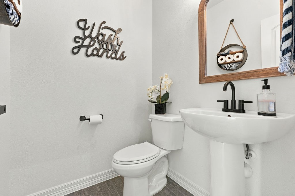Charming and compact half bathroom featuring a sleek pedestal sink, modern faucet, and decorative mirror. Stylish wall art and convenient storage add personality and practicality to the space.