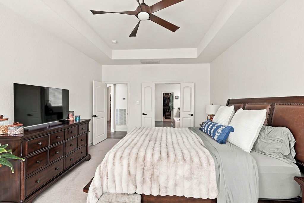 Spacious primary bedroom featuring a cozy bed, elegant dark wood furniture, and a modern ceiling fan, all complemented by soft, neutral walls for a tranquil retreat.
