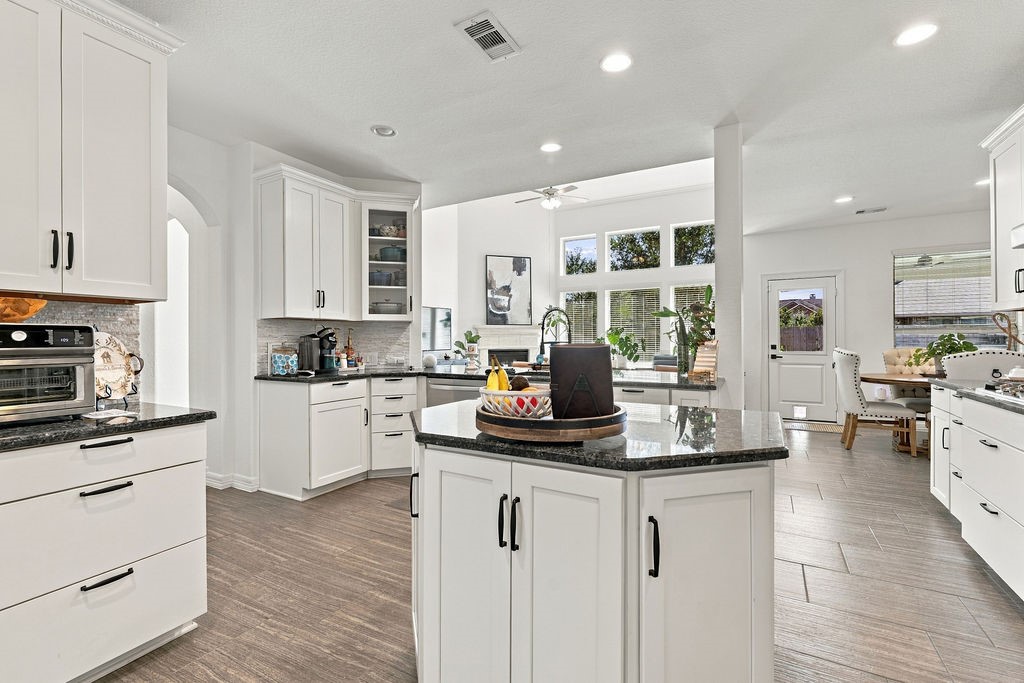 Spacious kitchen featuring sleek white cabinetry, granite countertops, and abundant natural light, seamlessly flowing into a cozy dining area.