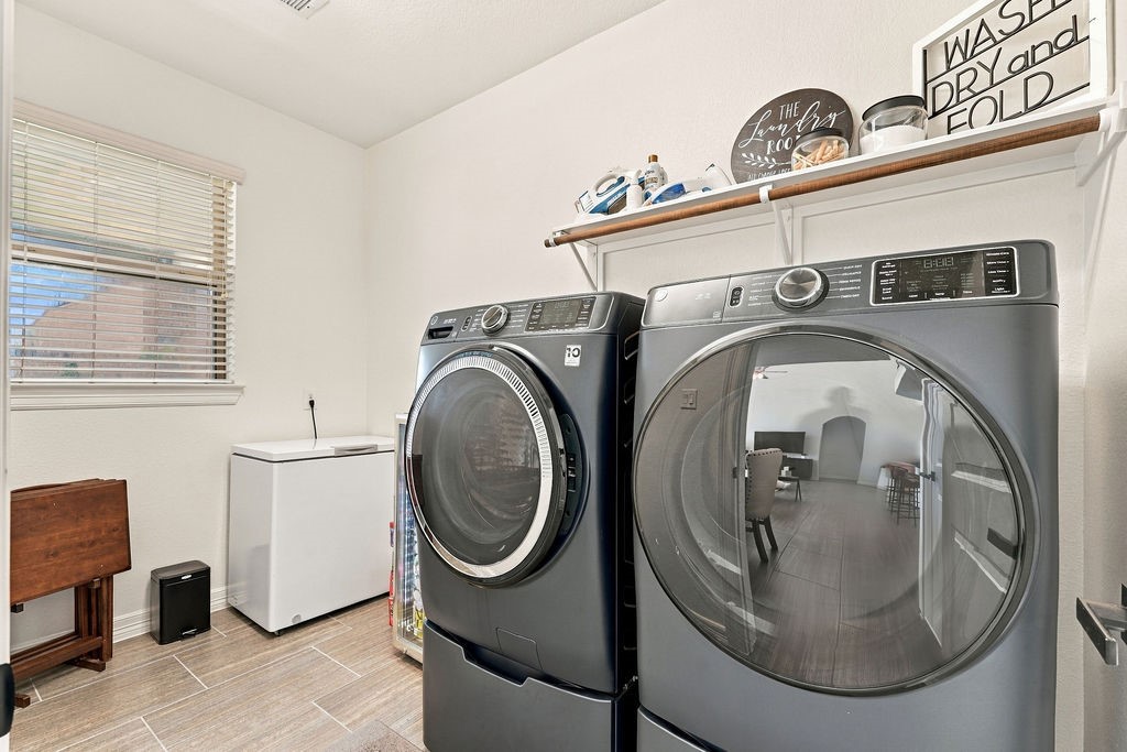 Spacious laundry room featuring modern washer and dryer, ample shelving for storage, and natural light from a large window.