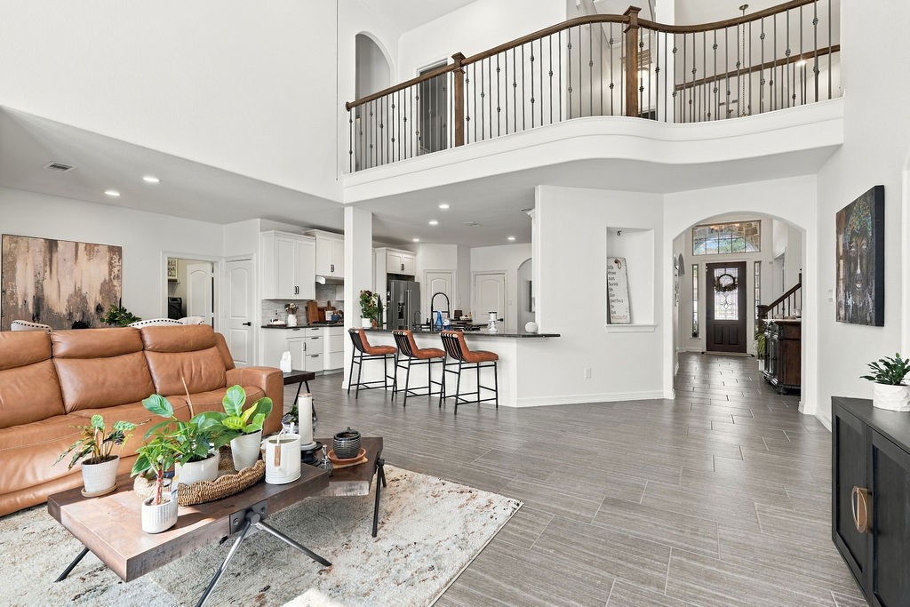 Spacious open-concept living area with high ceilings, featuring a modern kitchen with a breakfast bar, elegant wood-look flooring, and a grand staircase with a stylish railing.