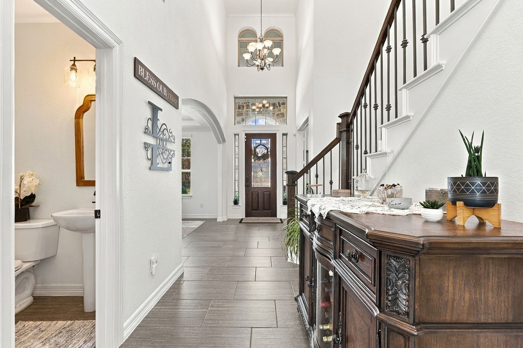 Elegant entryway with a grand staircase, high ceilings, and a welcoming chandelier. The space leads to a bright interior, creating a warm first impression.