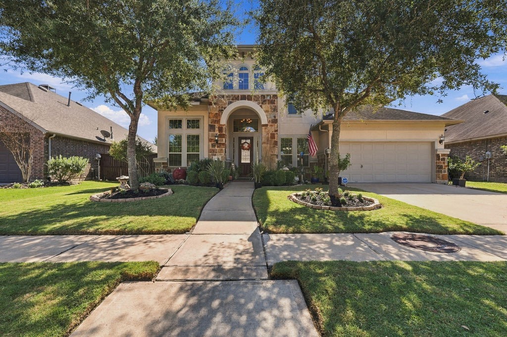 Stunning two-story home with a stone-accented facade, framed by mature trees and manicured landscaping, featuring a spacious driveway and welcoming entryway.