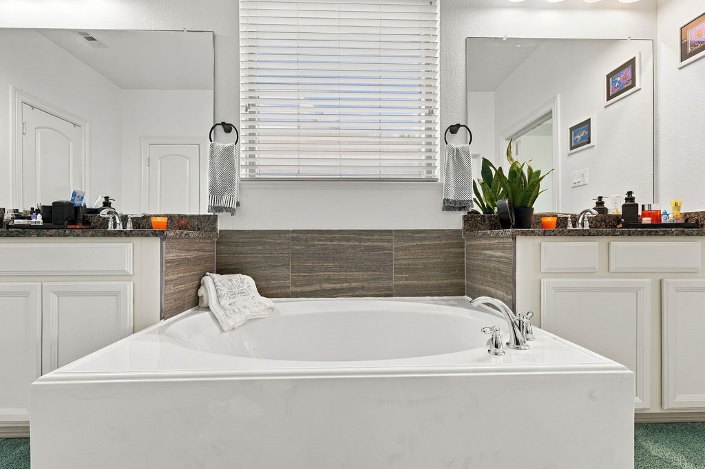 Luxurious bathroom featuring a spacious soaking tub, dual vanities with elegant granite countertops, and modern finishes, creating a serene retreat.