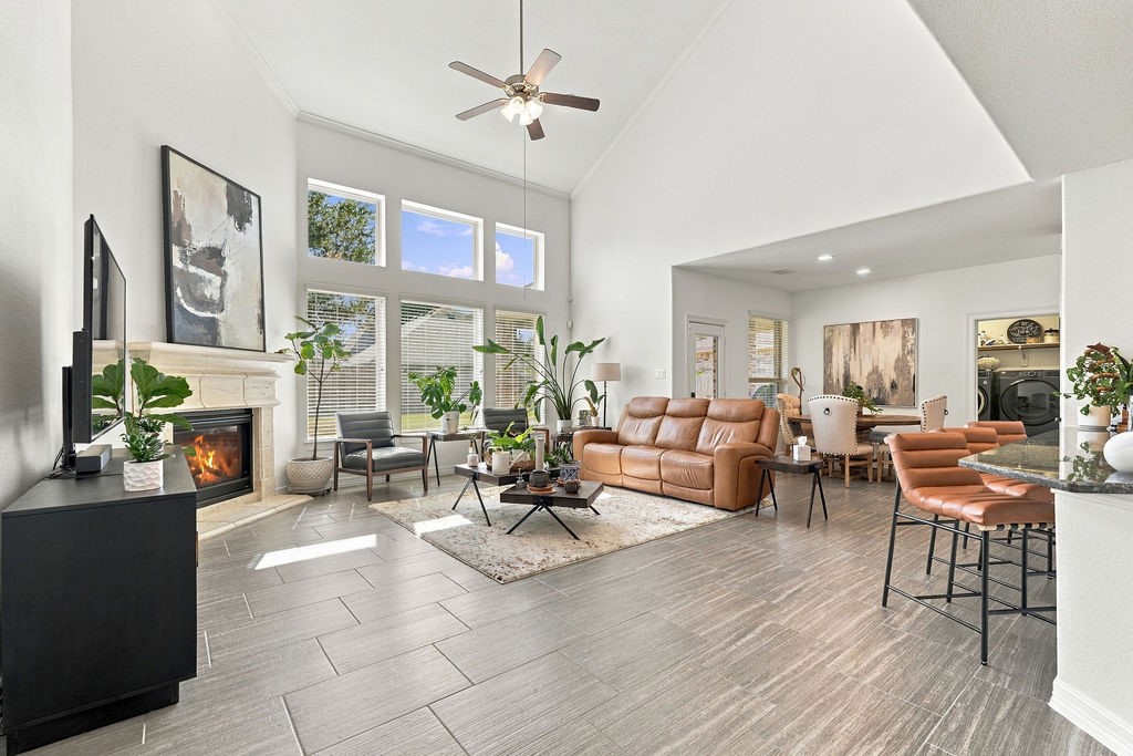 Spacious living area with high ceilings, abundant natural light from large windows, and a cozy fireplace. The open layout connects seamlessly to the dining and kitchen areas, offering a perfect setting for entertaining or relaxing.