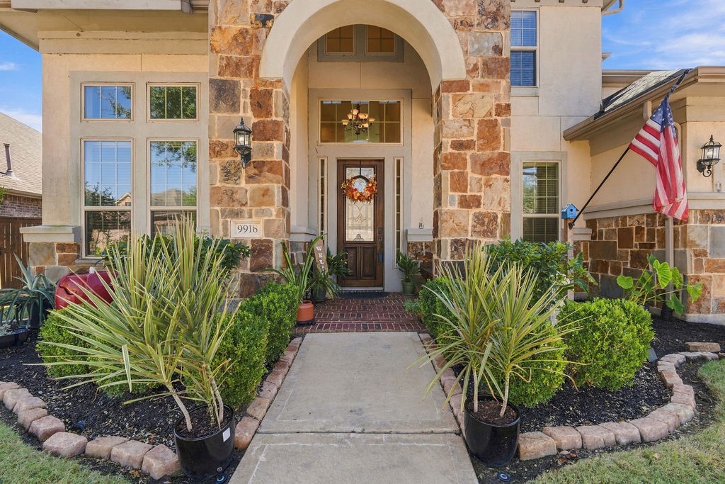 Charming stone-accented entryway with lush landscaping, welcoming front door, and elegant archway, creating a warm and inviting first impression.