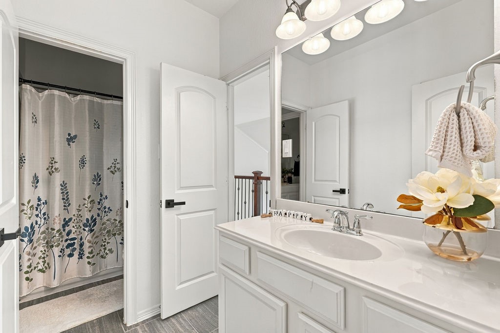 Bright and inviting bathroom featuring a spacious vanity with a large mirror, elegant light fixtures, and a charming floral shower curtain.