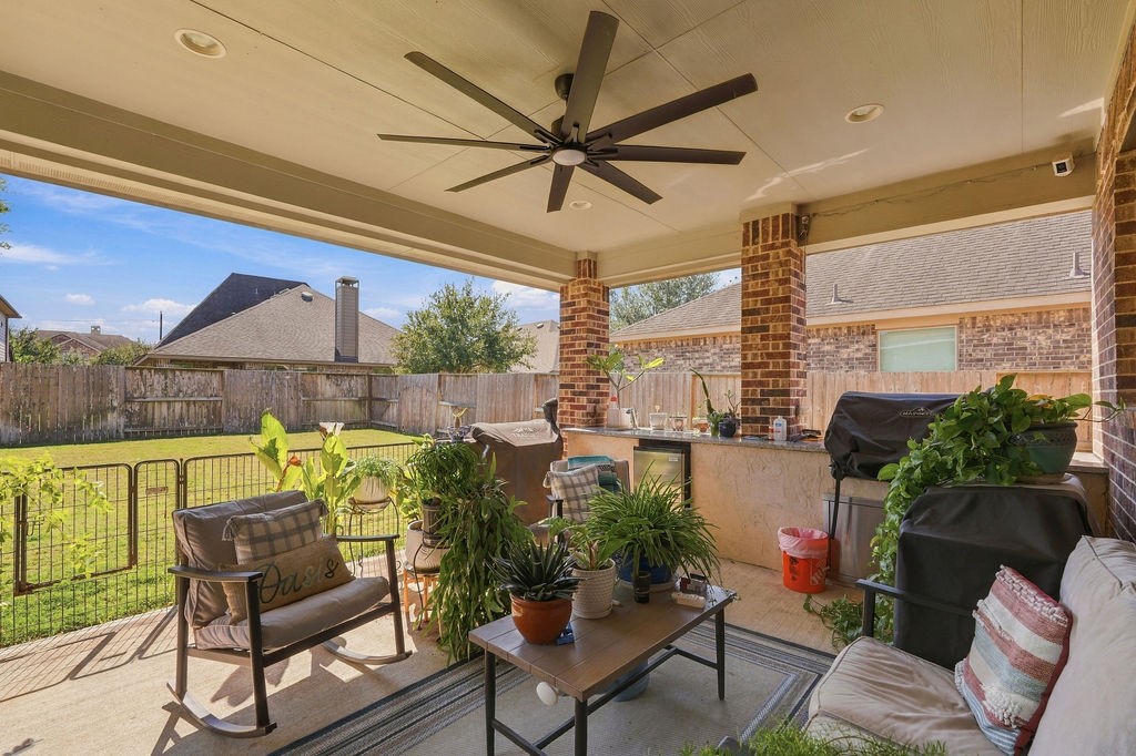 Charming covered patio perfect for relaxing and entertaining, featuring ceiling fan, outdoor seating, and built-in kitchen, all overlooking a spacious fenced backyard.