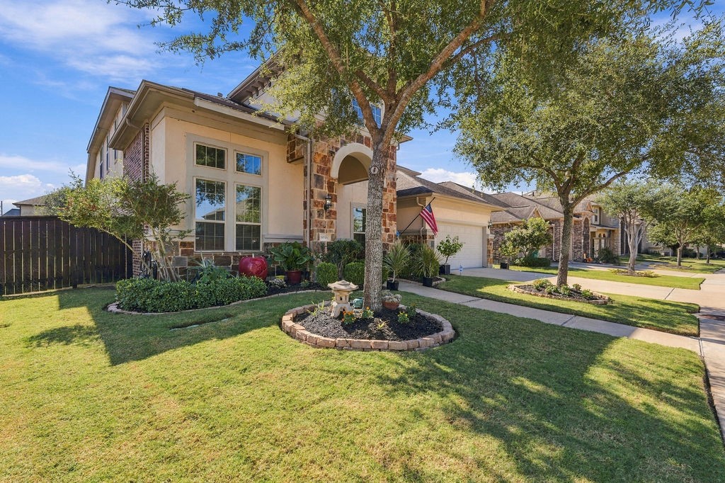 Charming home with a stone-accented facade, well-manicured lawn, and inviting front garden, nestled in a peaceful neighborhood.