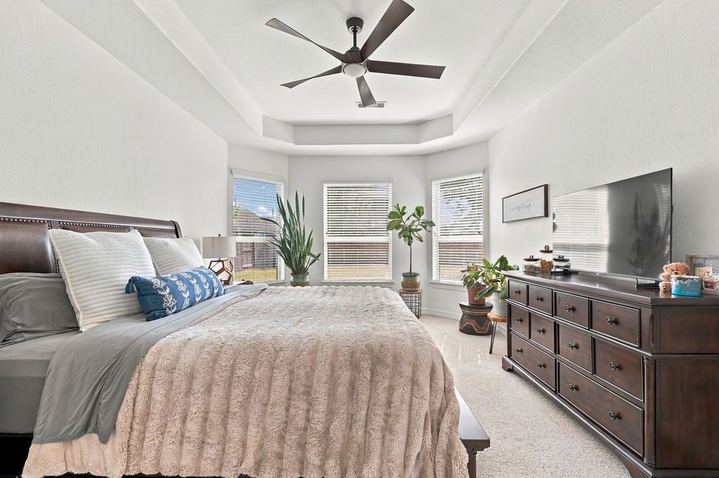 Spacious master bedroom with a cozy atmosphere, featuring a plush bed, large windows for ample natural light, and elegant ceiling fan.