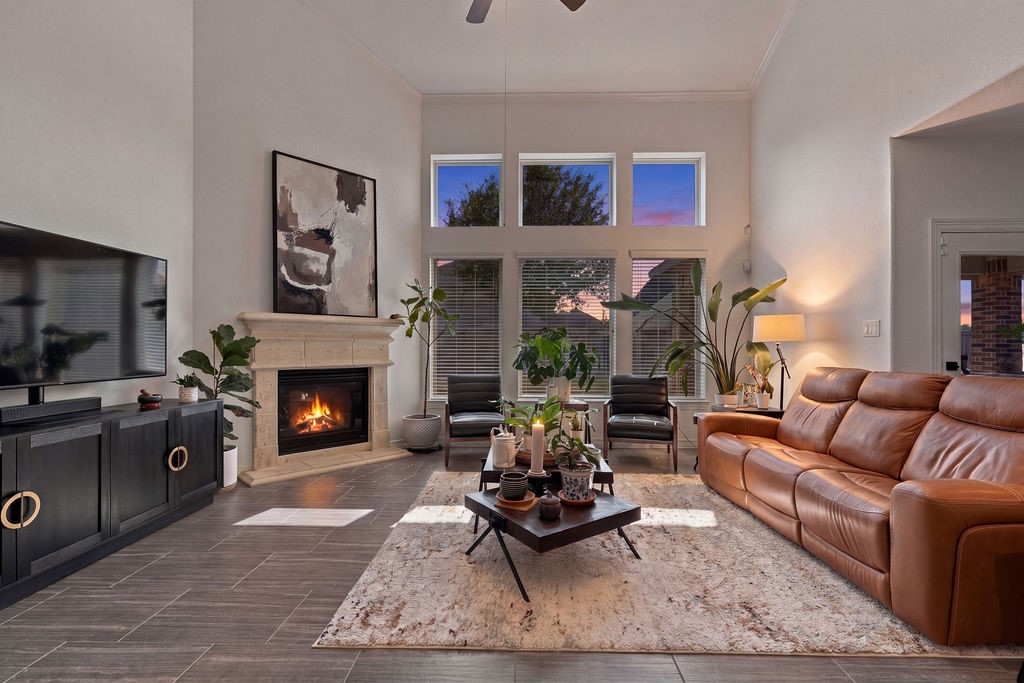 Spacious living room with high ceilings and large windows showcasing a stunning sunset view. Features a cozy fireplace, elegant tile flooring, and ample space for large furniture.