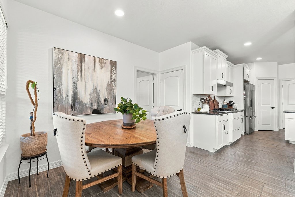 Bright and inviting kitchen with modern white cabinetry, stainless steel appliances, and a cozy dining area featuring a round wooden table and upholstered chairs. Seller is selling this set also.