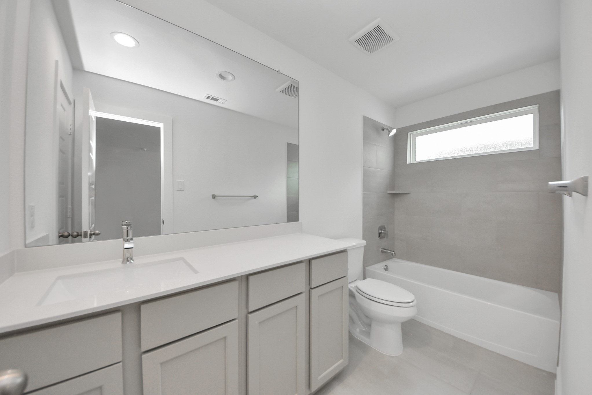 Secondary bath features tile flooring, bath/shower combo with tile surround, light stained wood cabinets, beautiful light countertop.