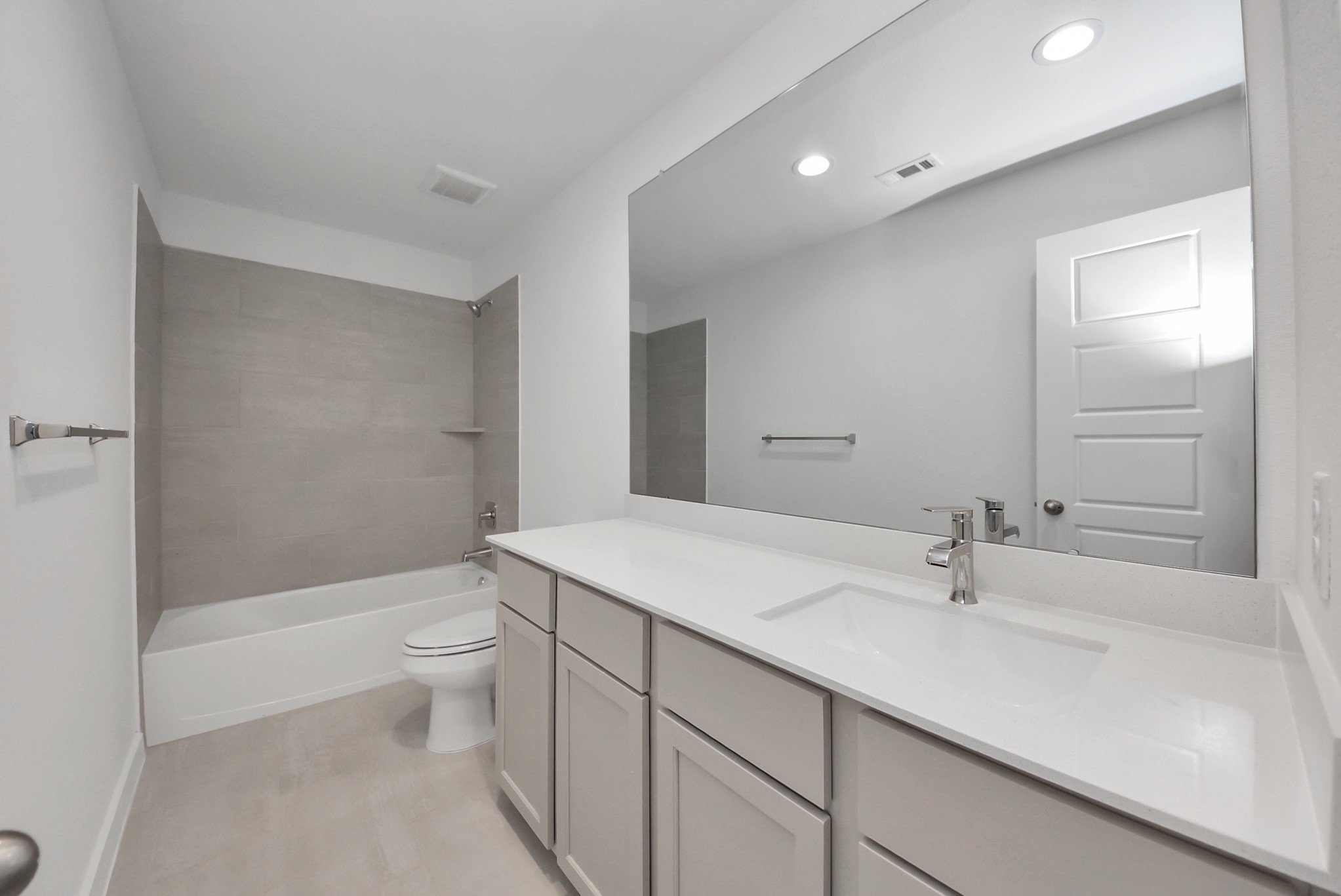 Secondary bath features tile flooring, bath/shower combo with tile surround, light stained wood cabinets, beautiful light countertop.
