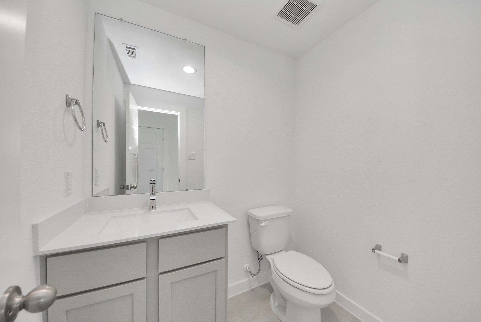 Sophisticated half bathroom adorned with contemporary finishes. The elegant 5-panel door welcomes you to a space where style meets functionality. Notice the sleek hardware accents that add a touch of modern charm. The vanity boasts light-colored countertops, beautifully complemented by a tasteful vanity light, creating a well-lit and inviting atmosphere.