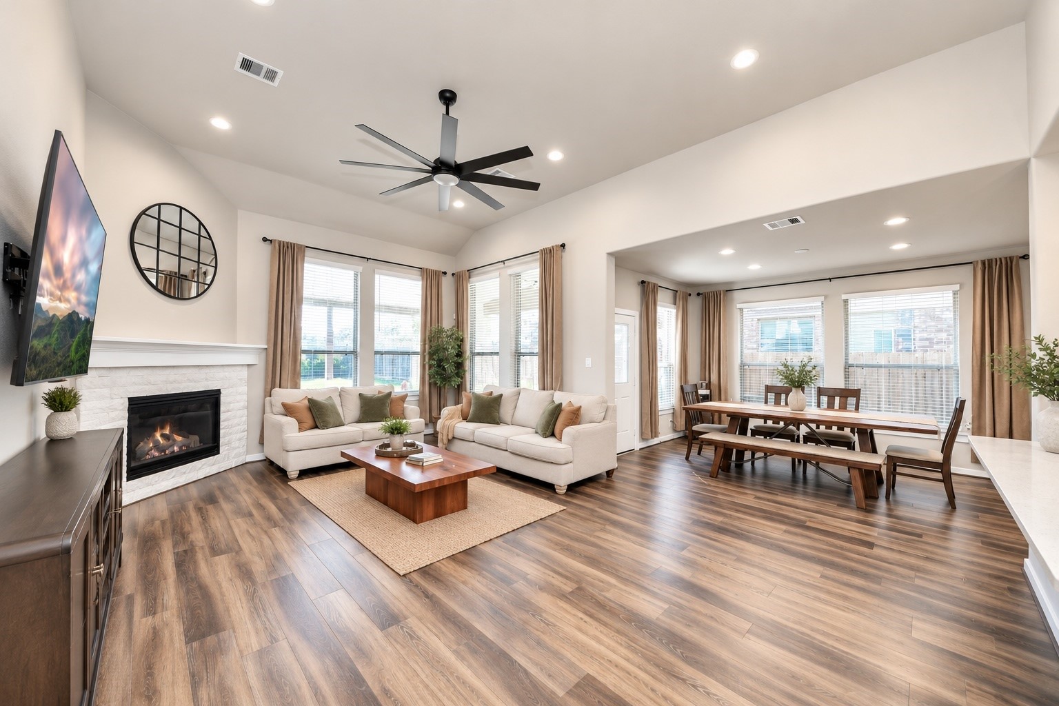 Inviting family room featuring soaring ceilings, expansive windows, a ceiling fan, and a gas fireplace that creates a welcoming gathering space.