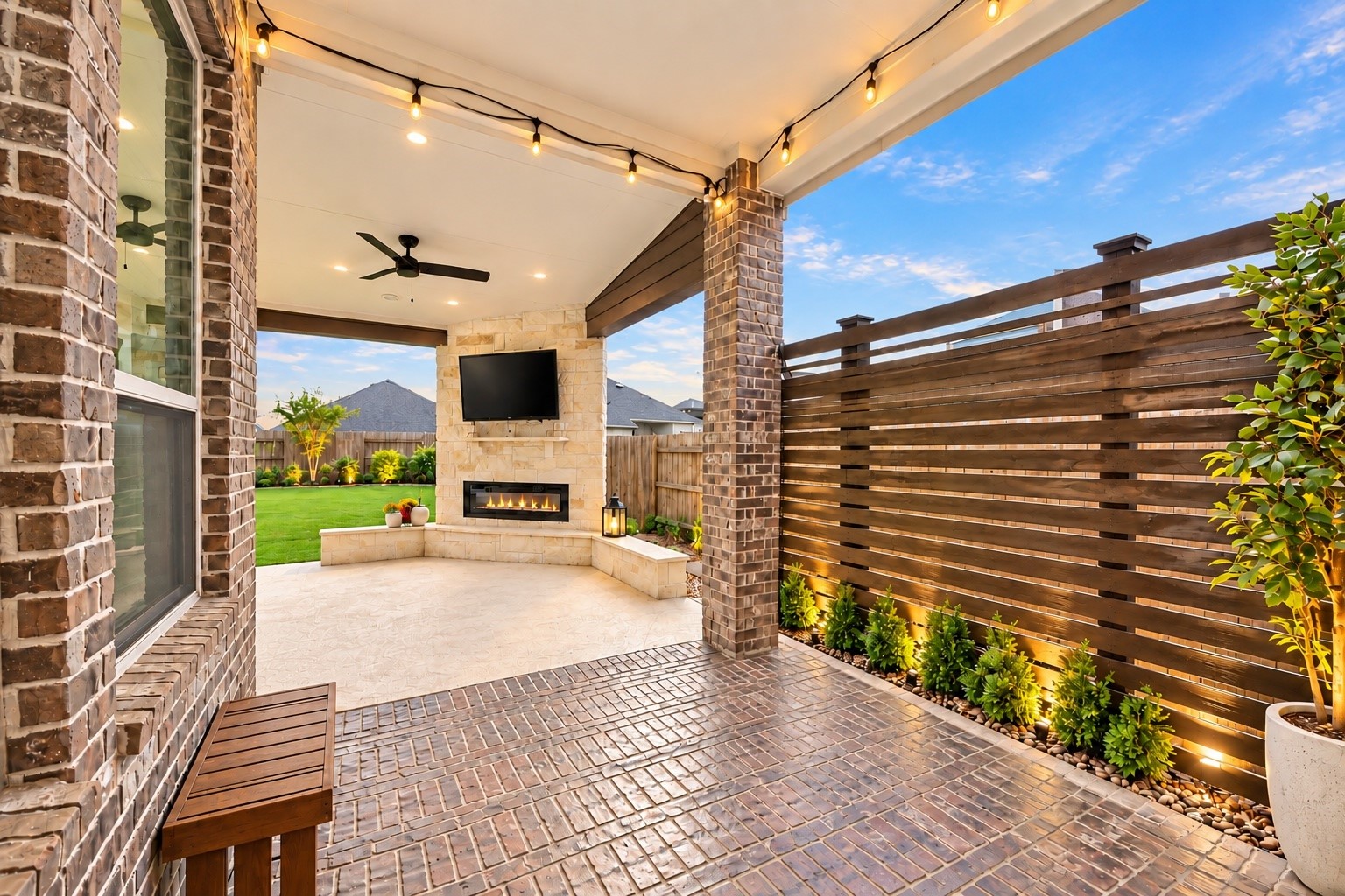 Additional view of the extended covered patio featuring brick flooring, overhead lighting, and a private fenced backyard.