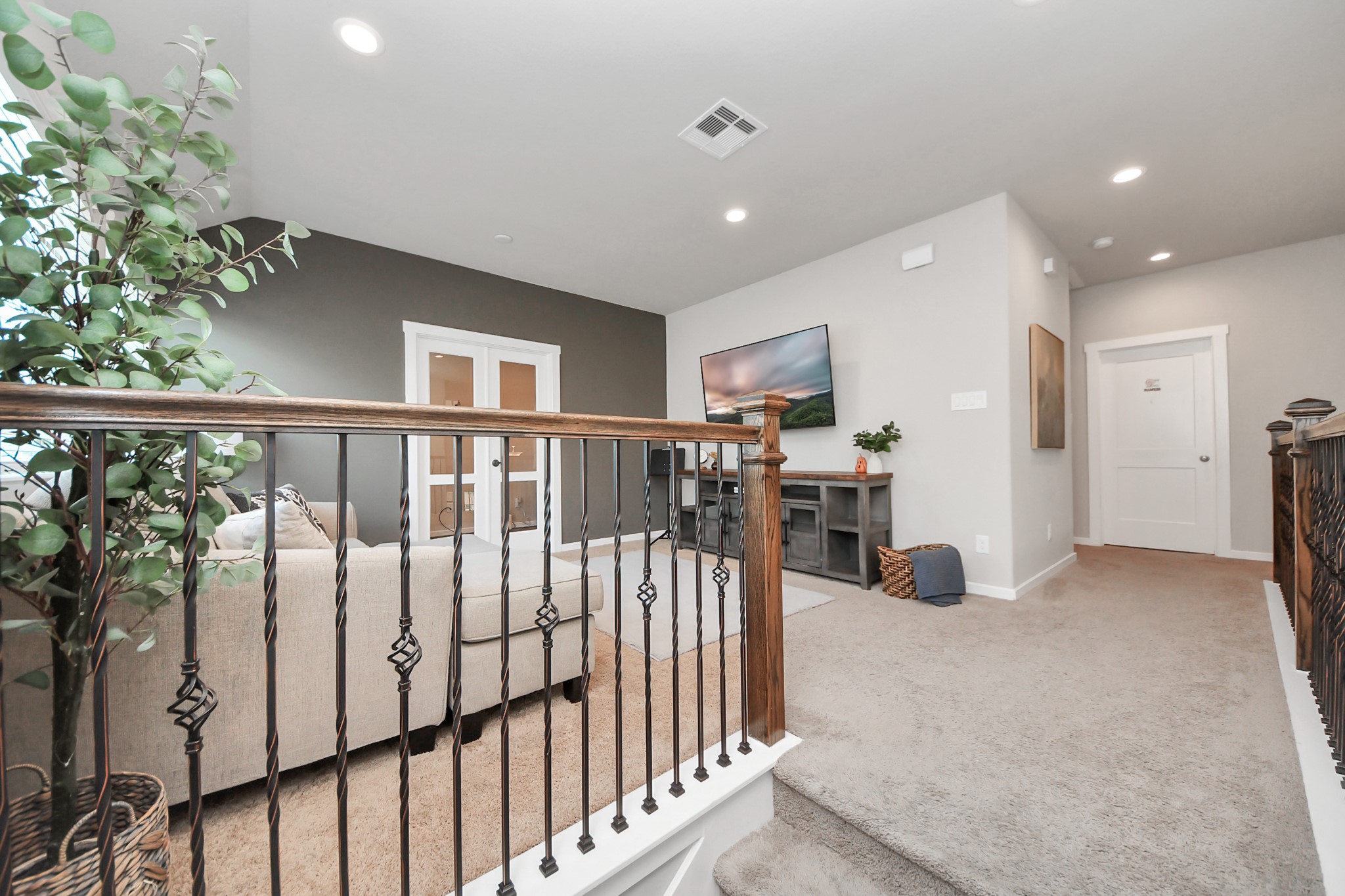 Open upstairs landing overlooking the main level, featuring wrought-iron railing and easy access to the secondary bedrooms and game room.