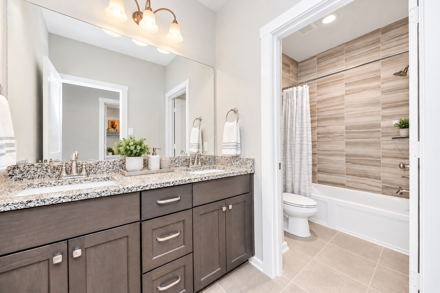 Full secondary bathroom with dual sinks, generous vanity storage, decorative lighting, and a tub/shower combination.